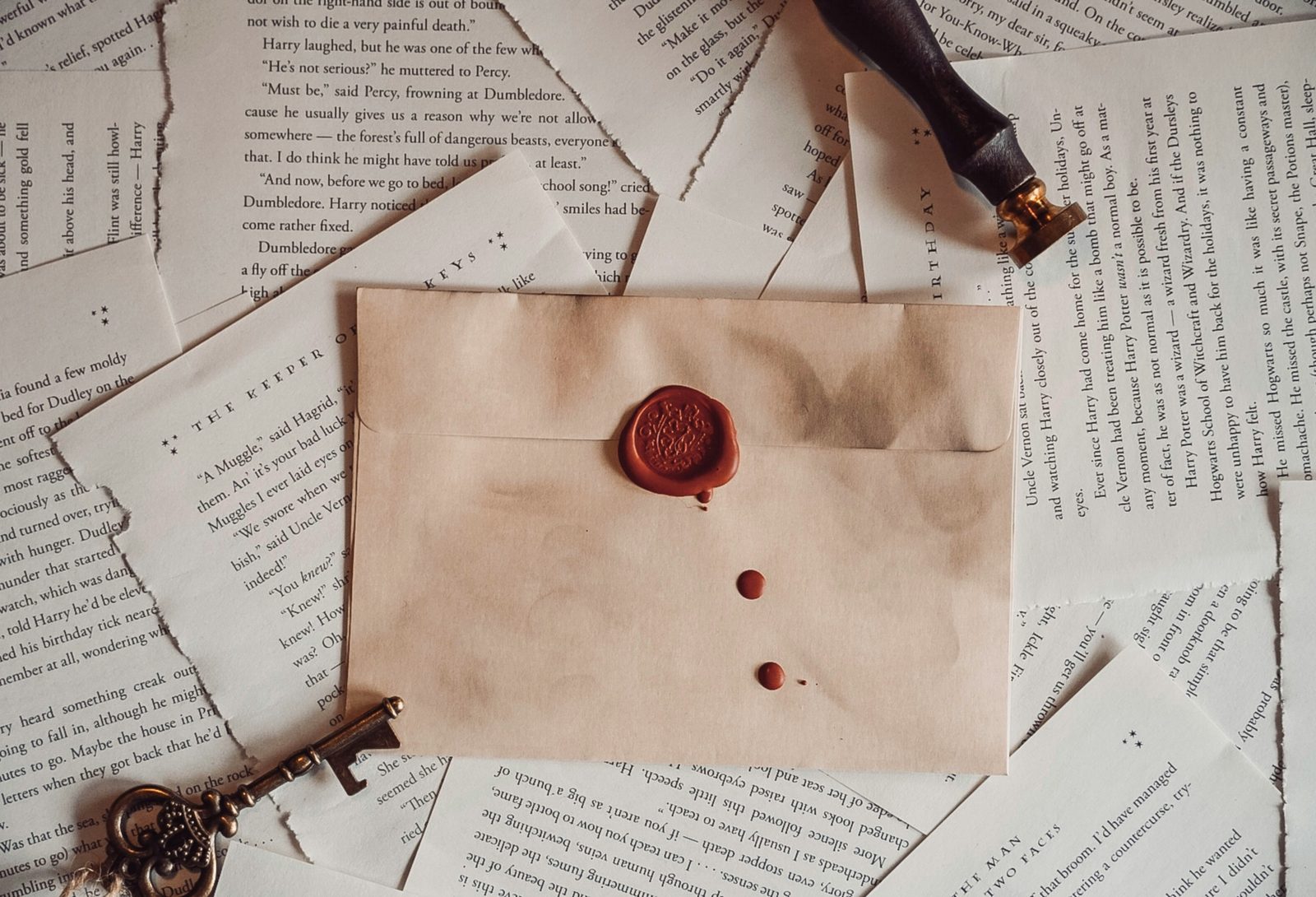 A wax-sealed envelope resting on torn book pages with a brass key